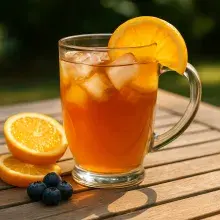 Eistee Früchtezauber auf Holztisch mit Eiswürfeln und Orangen