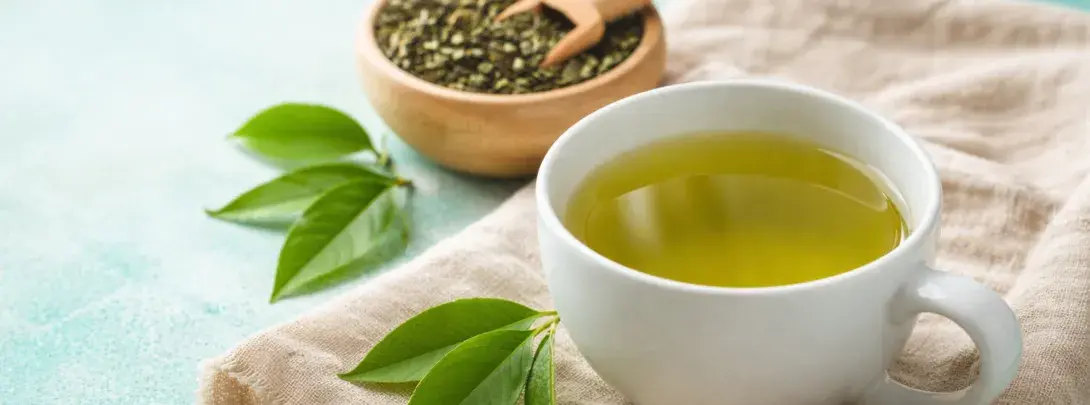 Weiße porzellantasse mit grünem tee, türkisener hintergrund und leinentuch